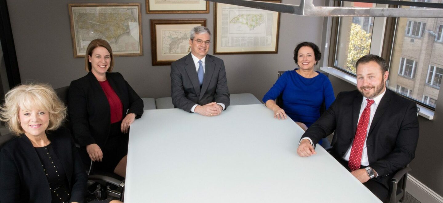 five formally dressed business people at a table smaller